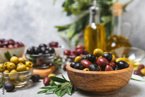 Set of green, red and black olives on a blue background. Different types of olives in bowls and olive oil with fresh olive leaves. Delicacy.Mediterranean Kitchen. Copy space.