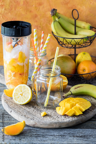 An empty glass jar mug with a straw waiting on a blended mango citrus smoothie.
