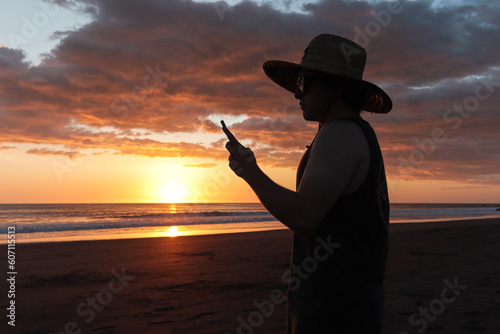 Image of a traveler on the beach of Tamarindo watching the orange and purple sunset meditating  taking pictures and enjoying the sound of the sea and the warmth of the sunset in Costa Rica.