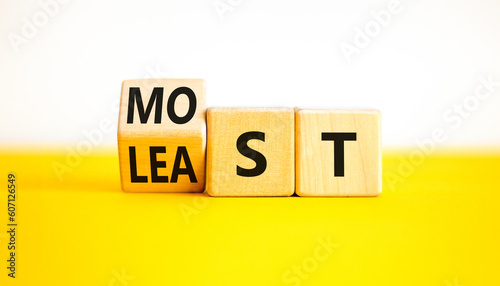 Most or least symbol. Businessman turns wooden cubes and changes the word Least to Most. Beautiful yellow table white background. Copy space. Business and most or least concept.