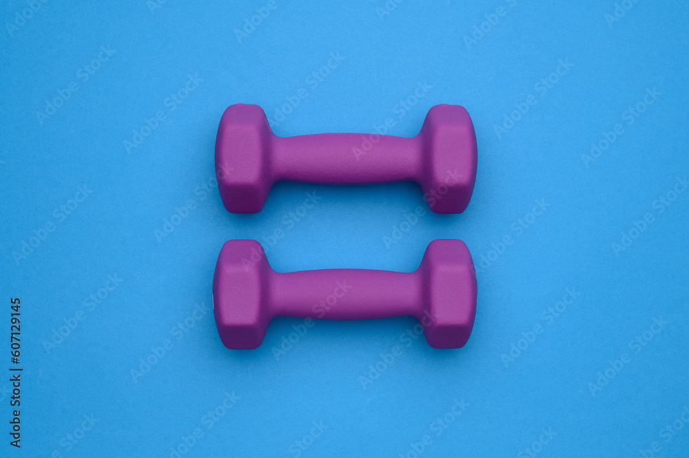 The layout of two rubberized dumbbells of 2 kg of purple color on a blue background, top view.Sports training The layout of two rubberized dumbbells of 2 kg of purple color on a blue background, top view.Sports training