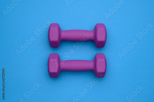 The layout of two rubberized dumbbells of 2 kg of purple color on a blue background, top view.Sports training