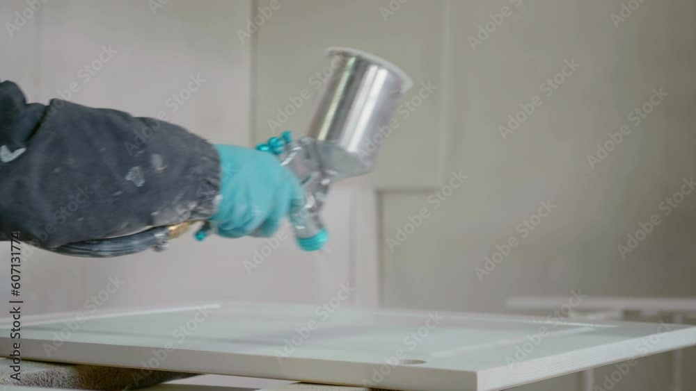 Close-up of a female carpenter's hands spraying varnish using compressed air on a wooden cabinet top. Furniture manufacture working process.