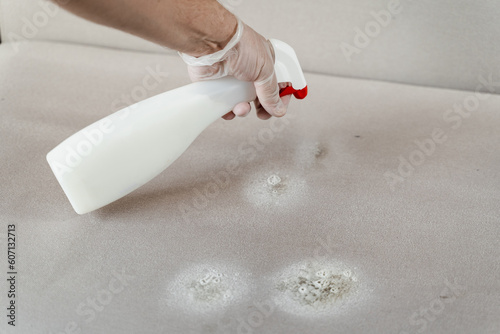 Cleaner is spraying dry cleaning chemicals detergent to clean and remove spots and dirt from upholstered textile furniture and neutralize smell. photo