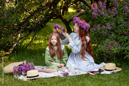 two sisters with long red hair at a picnic in a lilac garden