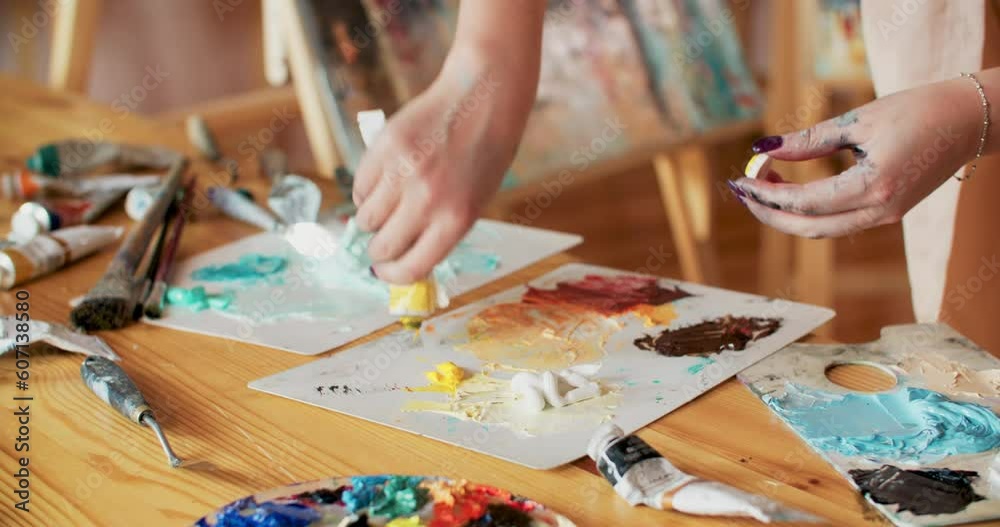 Woman artist mixing oil white and yellow paints on plastic palette using spatula. Professional creating painter preparing to draw on workplace in art workshop. Working in artistic studio with colours. Woman artist mixing oil white and yellow paints on plastic palette using spatula. Professional creating painter preparing to draw on workplace in art workshop. Working in artistic studio with colours.