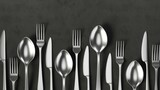A set of steel spoons, forks, and knives lie on a dark concrete surface