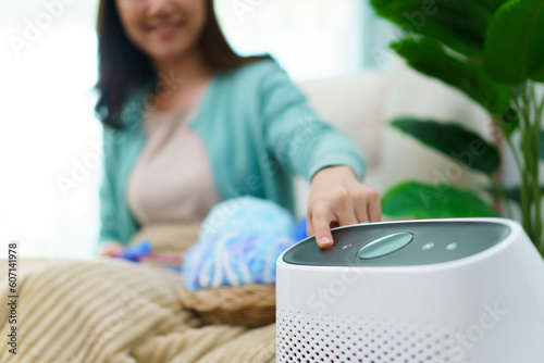 Happy Asian young woman turning on high efficiency air purifier while staying and relaxing in the living room. Woman using air purifier in her house.