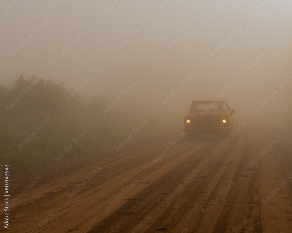 the silhouette of a pickup truck on a dirt road, during a foggy morning