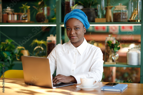 Pretty black lady student sitting at cafe, using laptop