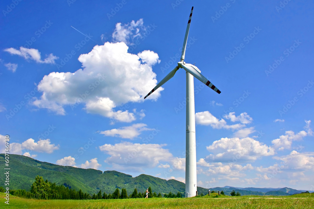 A single windmill in the foreground against a blue sky with white clouds and green mountains in the background, Rytro, Poland A single windmill in the foreground against a blue sky with white clouds and green mountains in the background, Rytro, Poland