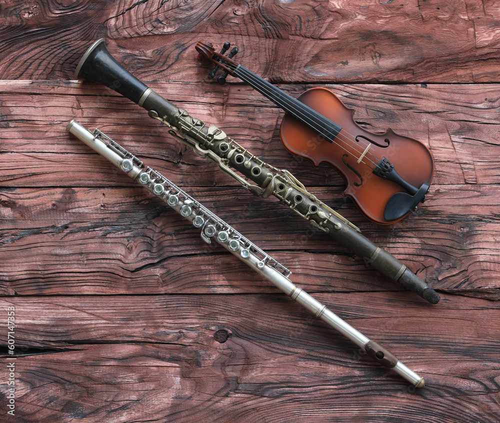 Naklejka premium violin, clarinet and flute on a red wooden table