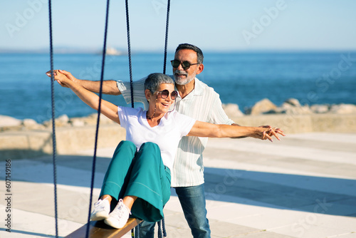 Cheerful Mature Couple Swinging At Sea Enjoying Summer Day Outdoors © Prostock-studio