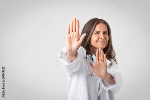 Reluctant and displeased senior woman doctor saying no, showing refusal gesture, telling to stop or stay away photo
