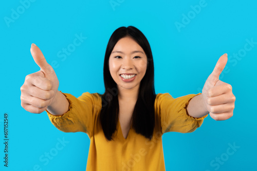 Positive young asian woman showing thumb ups and smiling © Prostock-studio