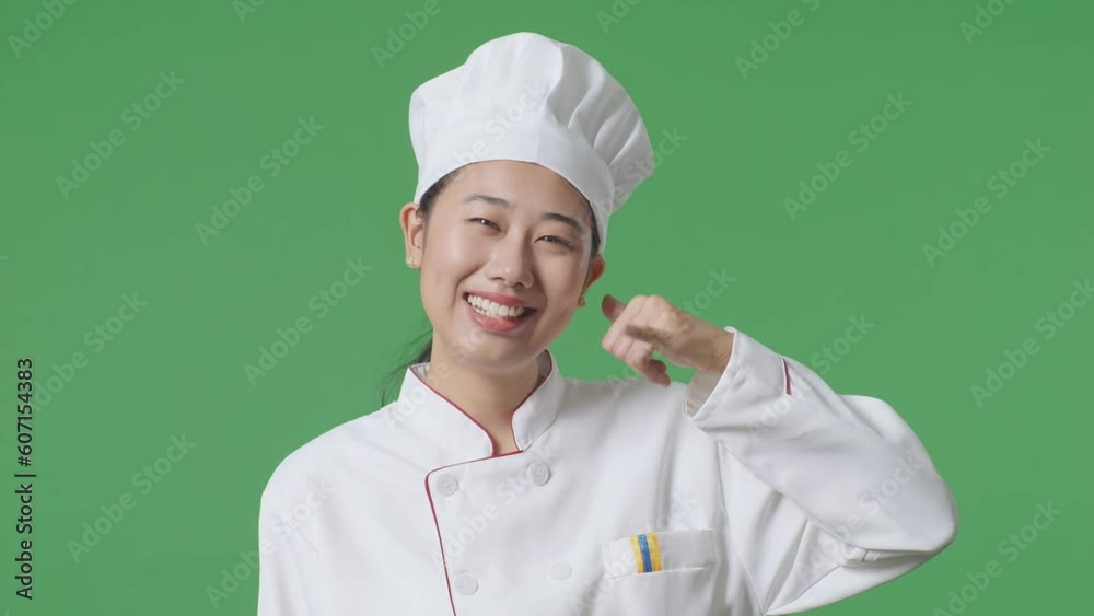 Close Up Of Asian Woman Chef Smiling And Making Call Me Gesture To Camera While Standing In The Green Screen Background Studio
