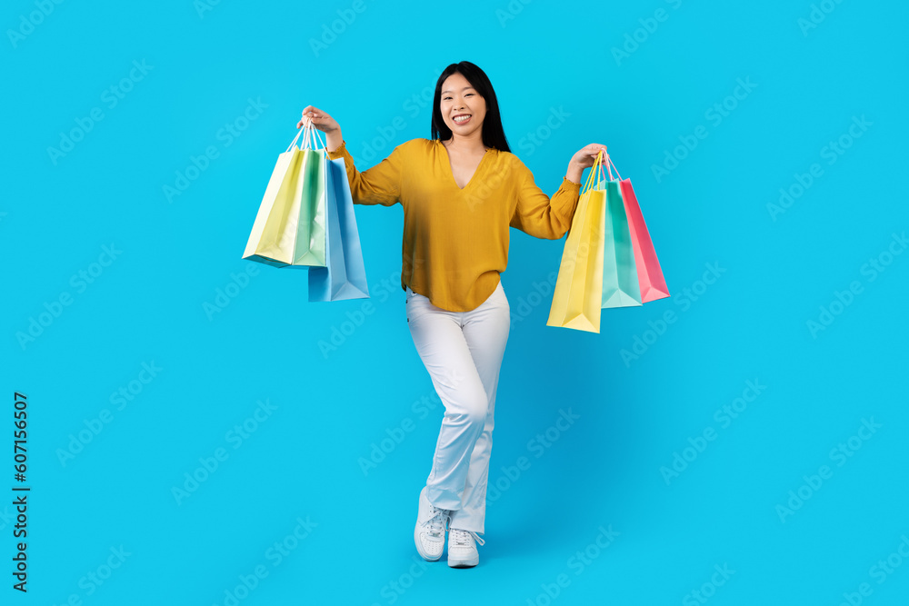 Positive young chinese lady showing shopping bags, blue background
