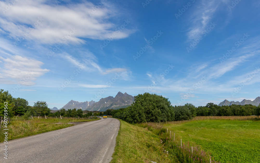 road behind which you can see the impressive landscape with mountains and lake on a round trip on the lofoten islands in 