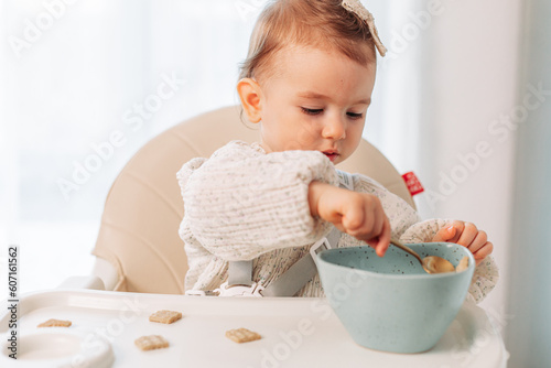 Little baby girl sitting in a highchair eating by herself with a spoon photo