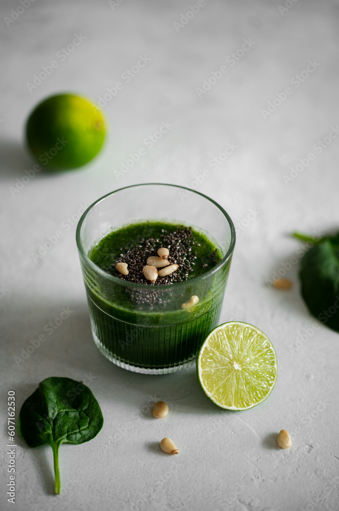 Fototapeta premium Green smoothie with spinach, banana, lime, chia seeds and pine nuts in a glass. Raw, vegan, vegetarian, healthy food concept