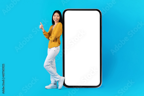 Beautiful asian young woman poisng by huge smartphone, mockup