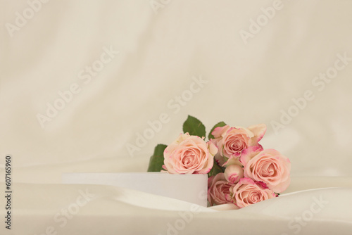 Fototapeta Naklejka Na Ścianę i Meble -  Pink rose flower bouquet on white podium and silk fabric.. Light beige background. Minimal empty display product presentation scene.