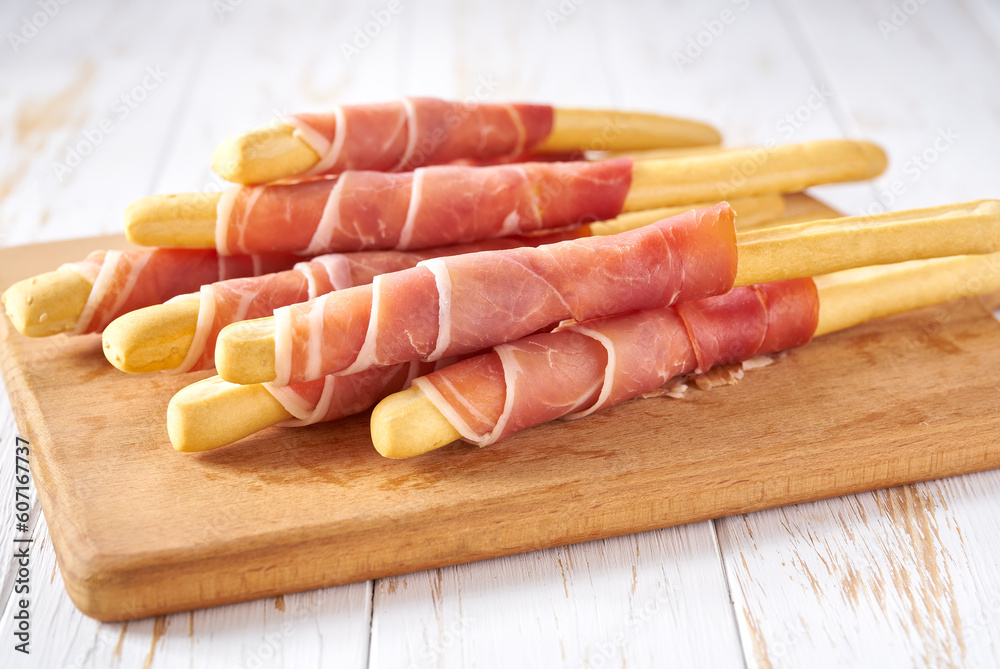 grissini or breadsticks with parma ham prosciutto on a white wooden table . grissini or breadsticks with parma ham prosciutto on a white wooden table .