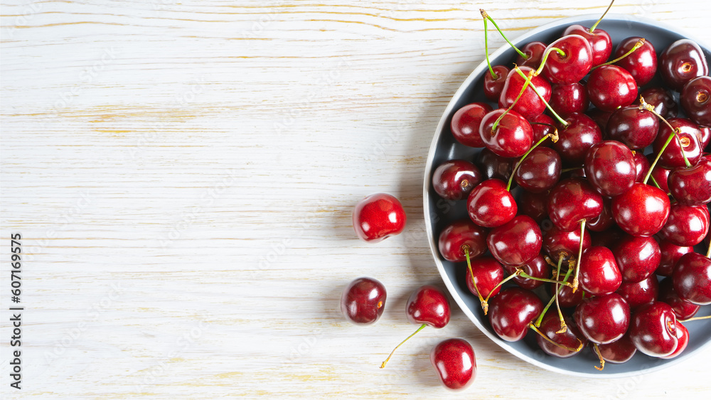 Fresh red ripe sweet cherry on plate on white wooden background. Berry, food background. Top view, banner, header with copy space. Fresh red ripe sweet cherry on plate on white wooden background. Berry, food background. Top view, banner, header with copy space.