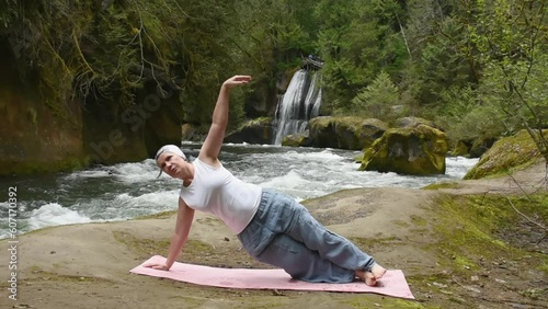 Middle-Aged Woman Practicing Yoga in front of a beautiful waterfall photo