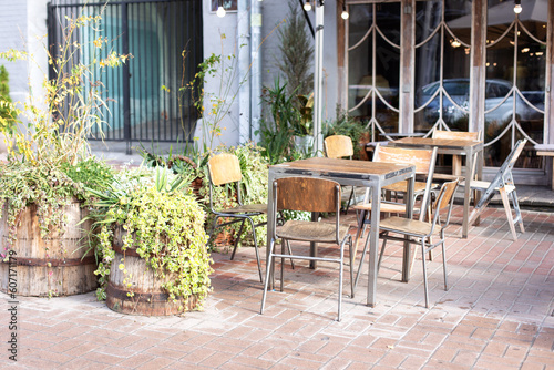 Typical view of Parisian street with tables of cafe and green plants in pots. Empty cafe with terrace with tables and chairs. Street vintage exterior of restaurant. Furniture for coffee shop in street