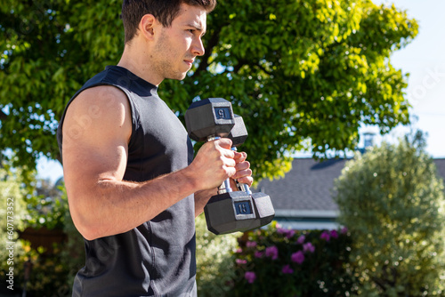 Young adult male doing bicep curls to target his arms during an afternoon at-home workout on a yoga mat during the coronavirus pandemic.