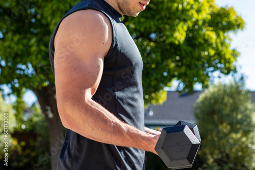 Young adult male doing bicep curls to target his arms during an afternoon at-home workout on a yoga mat during the coronavirus pandemic.