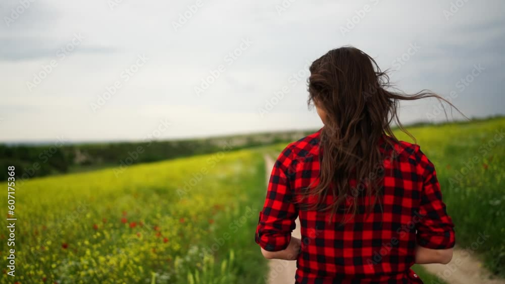 Woman field flowers. Rear view of woman walking in slow motion through a field. A woman is walking alone in a meadow field holding a bouquet of daisies, dressed in a red plaid shirt. Woman field flowers. Rear view of woman walking in slow motion through a field. A woman is walking alone in a meadow field holding a bouquet of daisies, dressed in a red plaid shirt.
