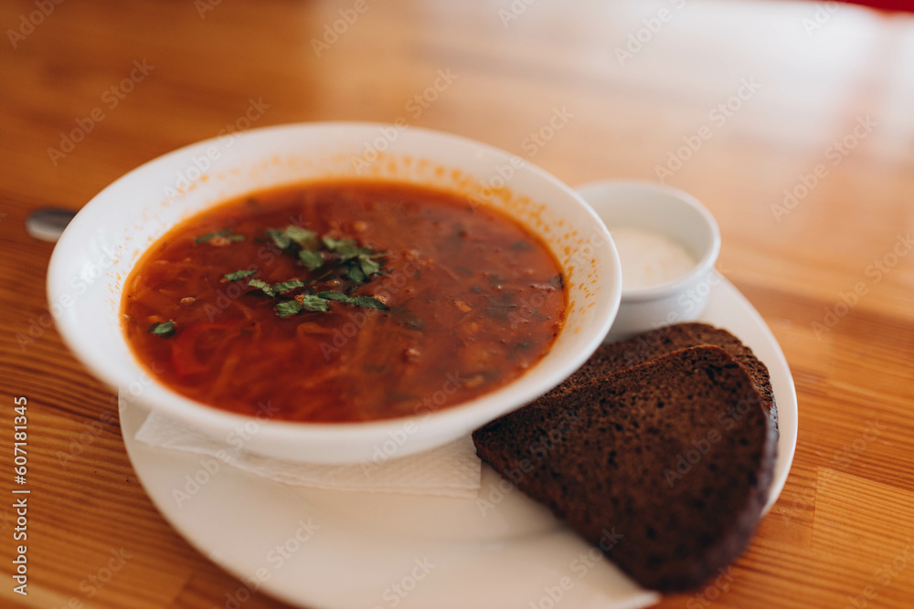 Traditional Ukrainian borsch. White Bowl of red beet root soup and greens. Sour delicious soup with potato, meat, carrot, cabbage, garlic. Traditional Ukraine food cuisine with brown bread, sour cream Traditional Ukrainian borsch. White Bowl of red beet root soup and greens. Sour delicious soup with potato, meat, carrot, cabbage, garlic. Traditional Ukraine food cuisine with brown bread, sour cream