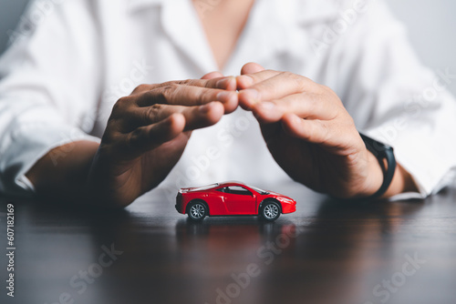 Business woman's hand protecting red toy car on desk. Planning to manage transportation finance costs. Concept of car insurance business, saving buy - sale with tax and loan for new car.