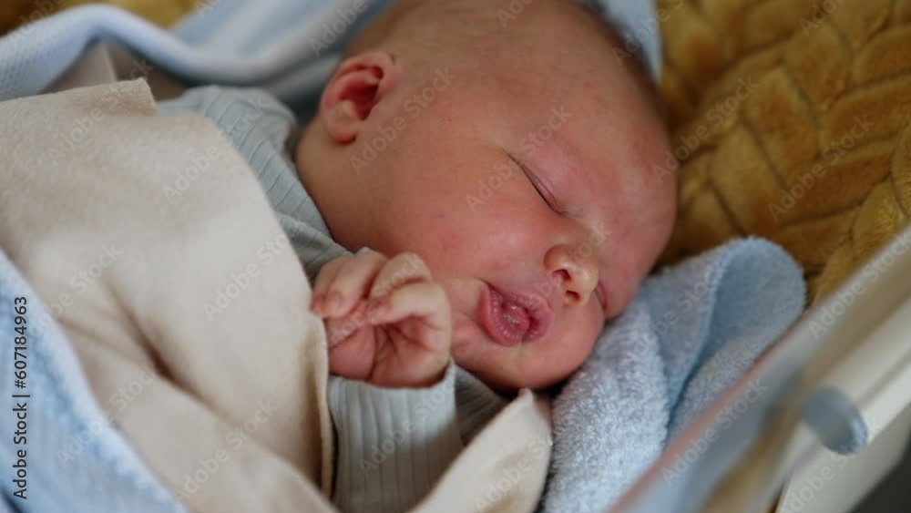 Few hours old infant waking up from his dream. Newborn starts to move in a crib and cry but dad's hands calms him down. Close up.