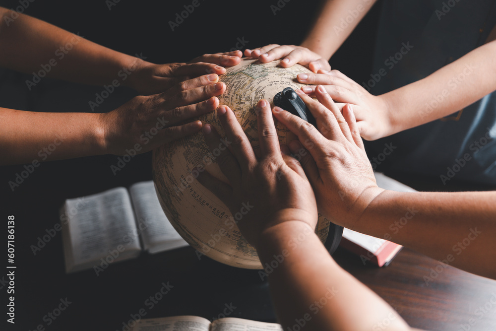 © doidam10 - Christian group praying for globe and people around the world on wooden table with bible. Christian small group praying together around a wooden table with bible page in homeroom.