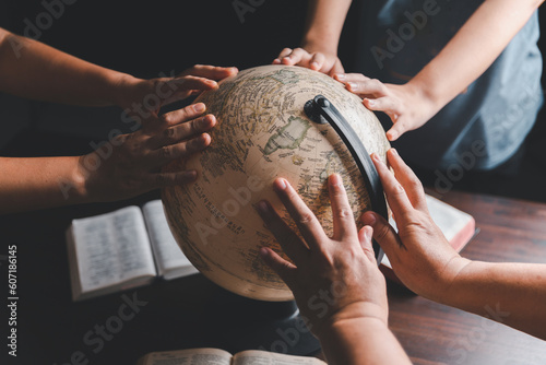 Christian group praying for globe and people around the world on wooden table with bible. Christian small group praying together around a wooden table with bible page in homeroom. photo