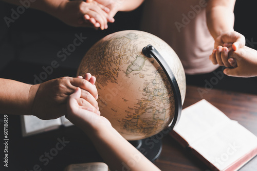 Christian group praying for globe and people around the world on wooden table with bible. Christian small group holding hands and praying together around a wooden table with bible page in homeroom.