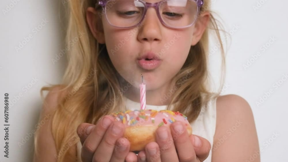 A girl child blowing out a candle on a pink donut. Happy Birthday or anniversary concept. A girl child blowing out a candle on a pink donut. Happy Birthday or anniversary concept.