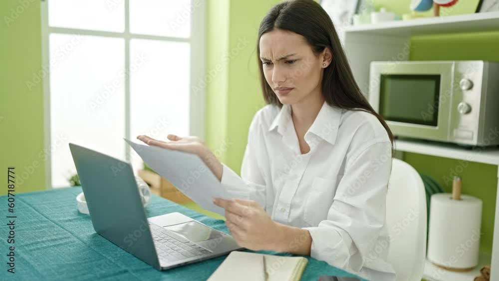 Young beautiful hispanic woman using laptop reading document at dinning room Young beautiful hispanic woman using laptop reading document at dinning room