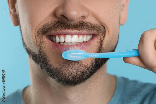 Man brushing his teeth with plastic toothbrush on light blue background, closeup