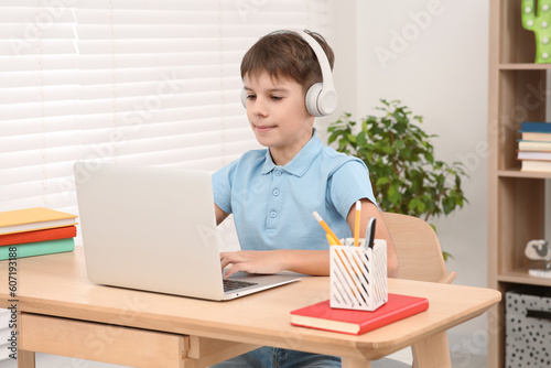 Boy using laptop and headphones at desk in room. Home workplace © New Africa