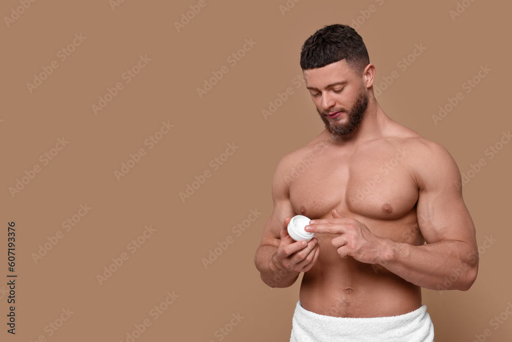 Handsome man applying body cream on pale brown background, space for text