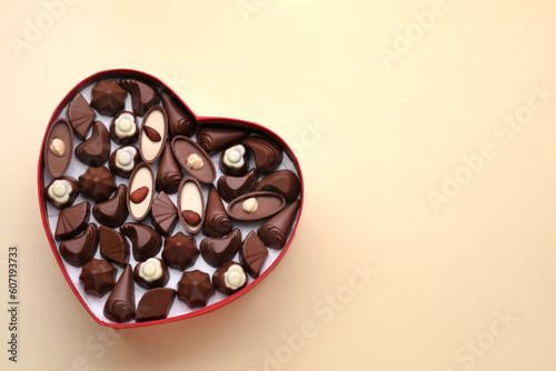 Heart shaped box with delicious chocolate candies on beige background, top view. Space for text © New Africa
