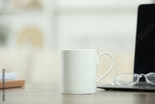 White ceramic mug, glasses and laptop on wooden table indoors. Space for text