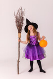 Happy beautiful little blonde girl witch with a broom and pumpkin pot on a white background