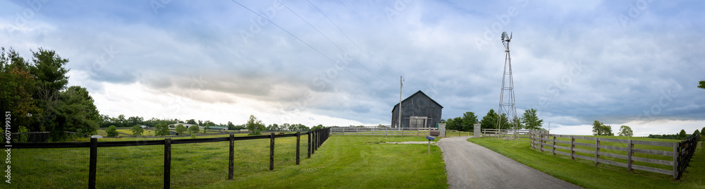 A picturesque scene of a Kentucky farm unfolds, showcasing a barn and a wind power generation tower standing alongside a fence in the rural panorama.