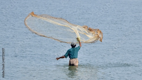 Man in blue shirt and gray shorts throwing a fish net in water