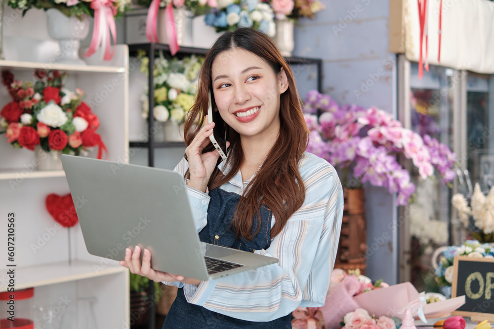 One young Asian female florist owner, working with laptop, selling floral arrange, talking on mobile phone in colorful flower shop store with a beautiful bunch of blossoms, and e-commerce business. - obrazy, fototapety, plakaty 
